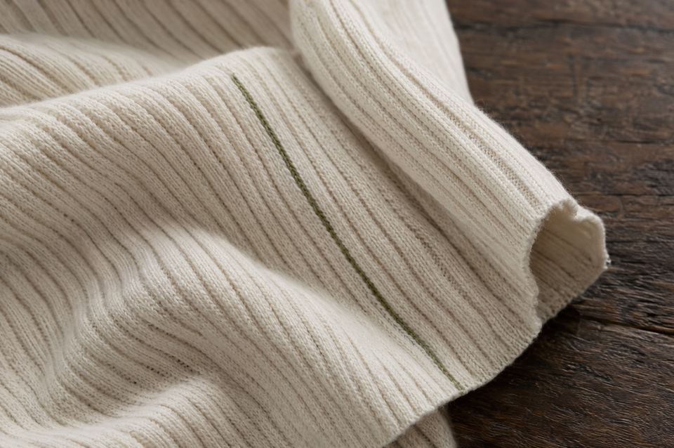Naturweißer Rippstrick aus Baumwolle mit einem eingestrickten olivgrünen Faden auf dunklem Holz