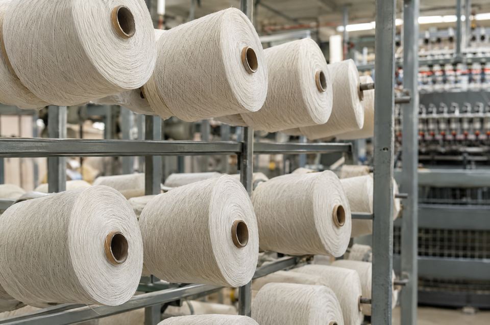 Naturweiße Open-End-Garnkonen auf einem Gestell vor der Spinnmaschine